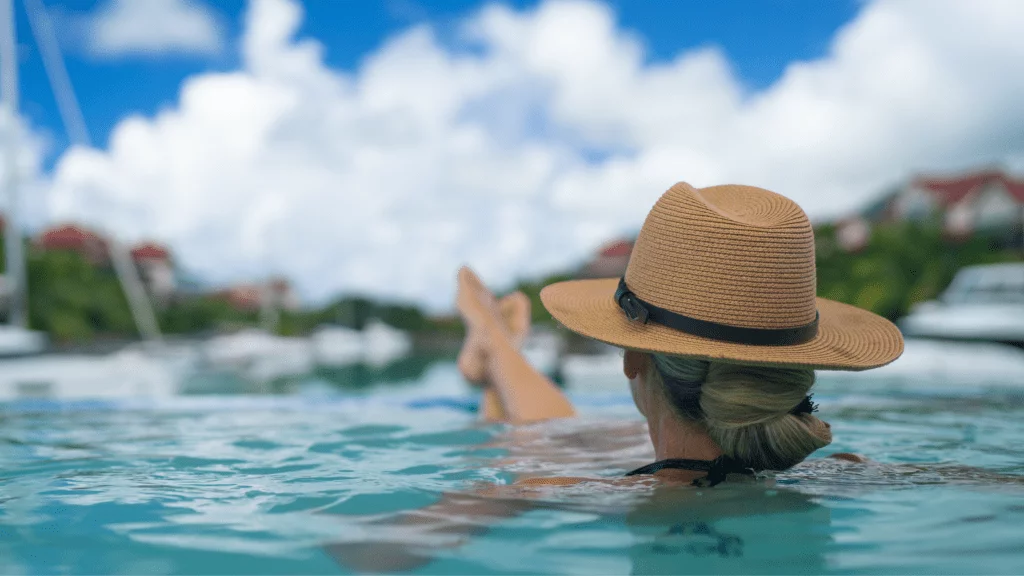 A woman in a sun hat floats leisurely in the sea, reflecting the financial competence and control that a Net Worth Mentor brings to achieving freedom, luxury, and leisure