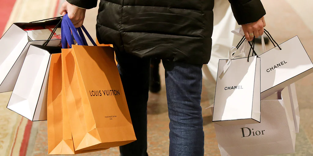 Woman carrying luxury-brand shopping bags: Vuiton, Chanel, and Dior—Luxury Industry market check visual.