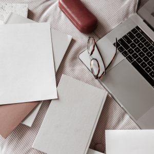 flatlay of a desk in cool tones showing a silver laptop , some glasses with a box and some white notepads - financially savvy women and the stock market
