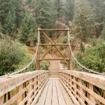 A wooden bridge stretches across a ravine in a mountainous landscape—symbolizing the journey to finding your Financial Voice and stepping onto a secure path ahead.