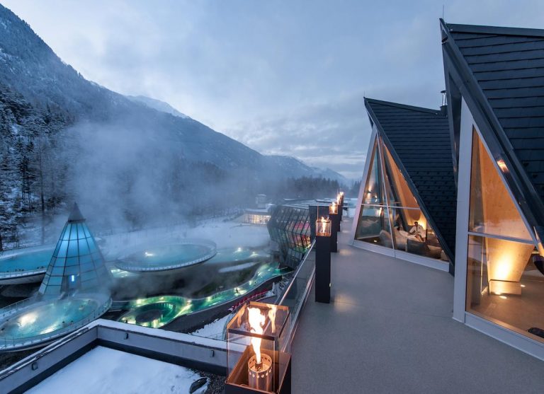 A mountain resort against the backdrop of mountains covered in snow, lanterns and several jacuzzis. The glow of open fireplaces is reflected in the window, depicting deep relaxation and serenity similar to the December-January curated Lettercurated to build confidence and help you become the most interesting woman in the room.
