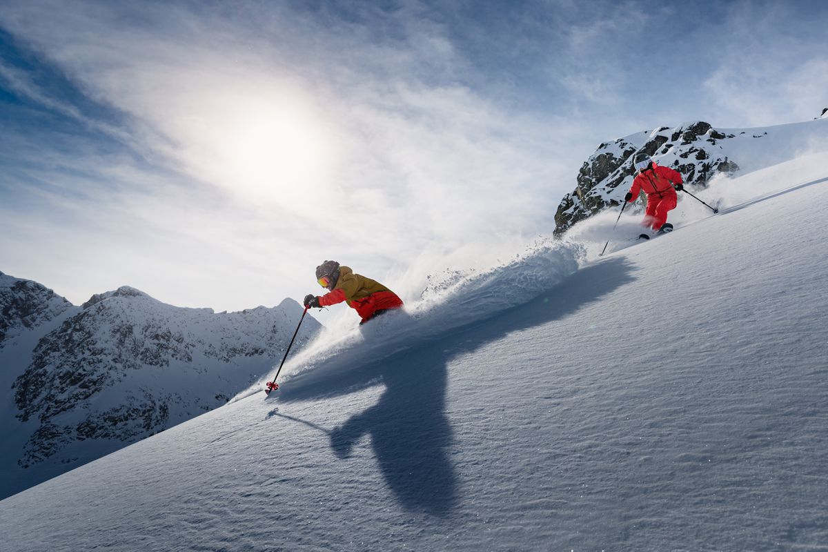 Curated Letter , February & March 2023 edition talks about the season's best ski resorts. The Image shows two people skiing downhill in fresh powder snow withelegant sophistication