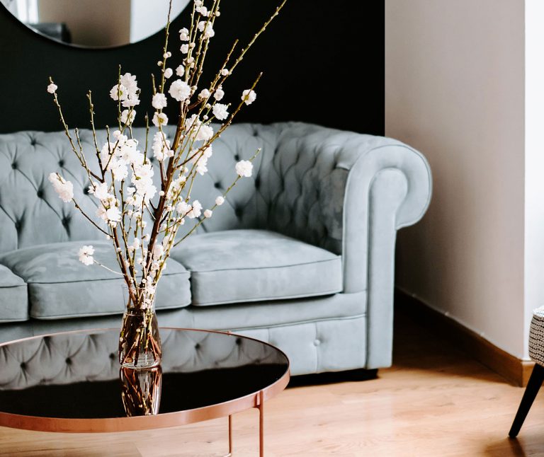 A duck-egg Chesterfield sofa and coffee table with flowers create an elegant, composed setting for a Women’s Guide on finding a Wealth Manager.