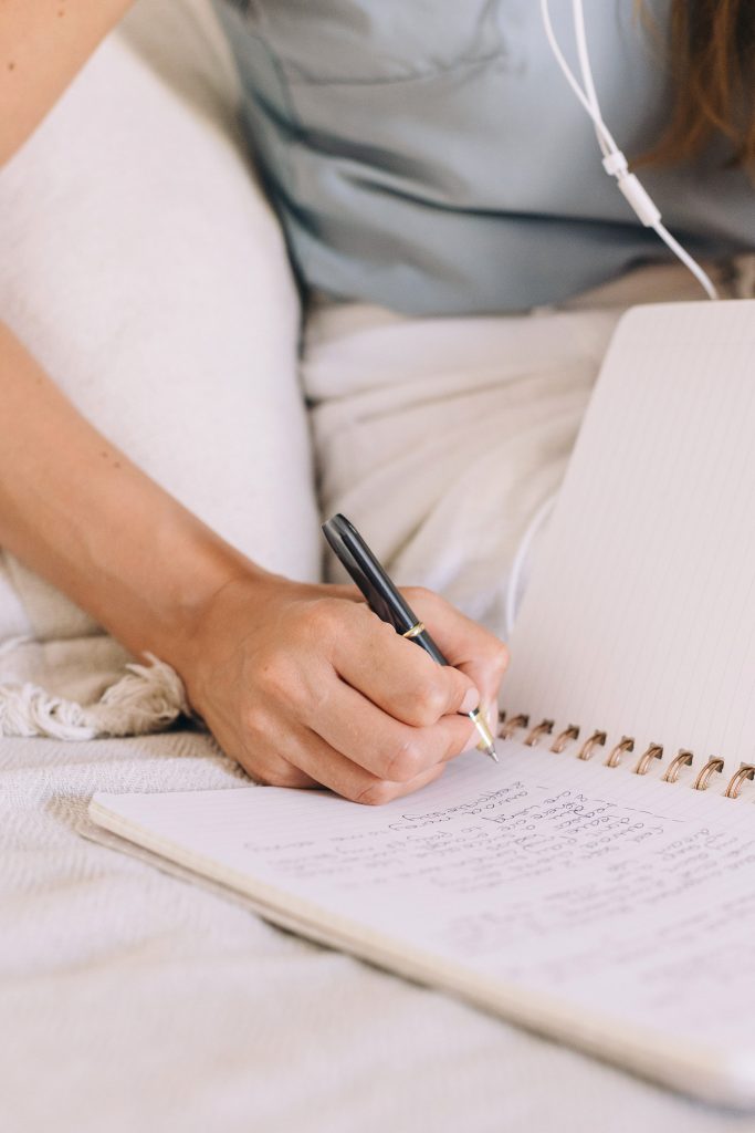 Woman with earphones lists questions to prepare her e-mail to Invest!ELLE. Who Can Help to amswer questions