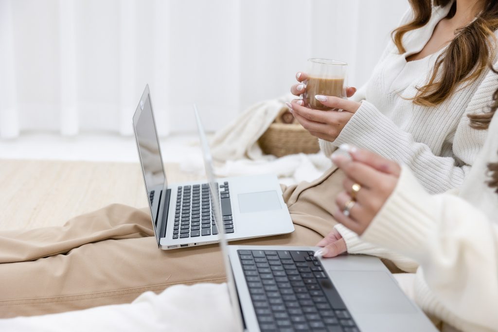 Female Friends sitting on a bed, each with a laptop, writing their emails to Invest! Elle´s "How Can I Help? 