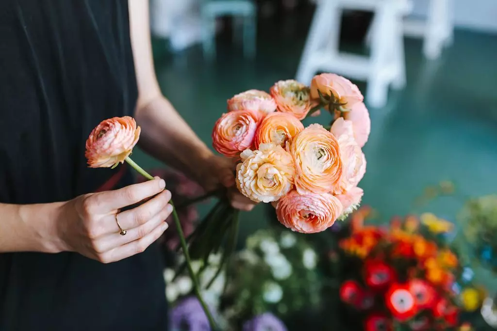 Woman arranging flowers , the visible elegance and choice pof paech and pink colored flowers symbolise carefully curated letters.